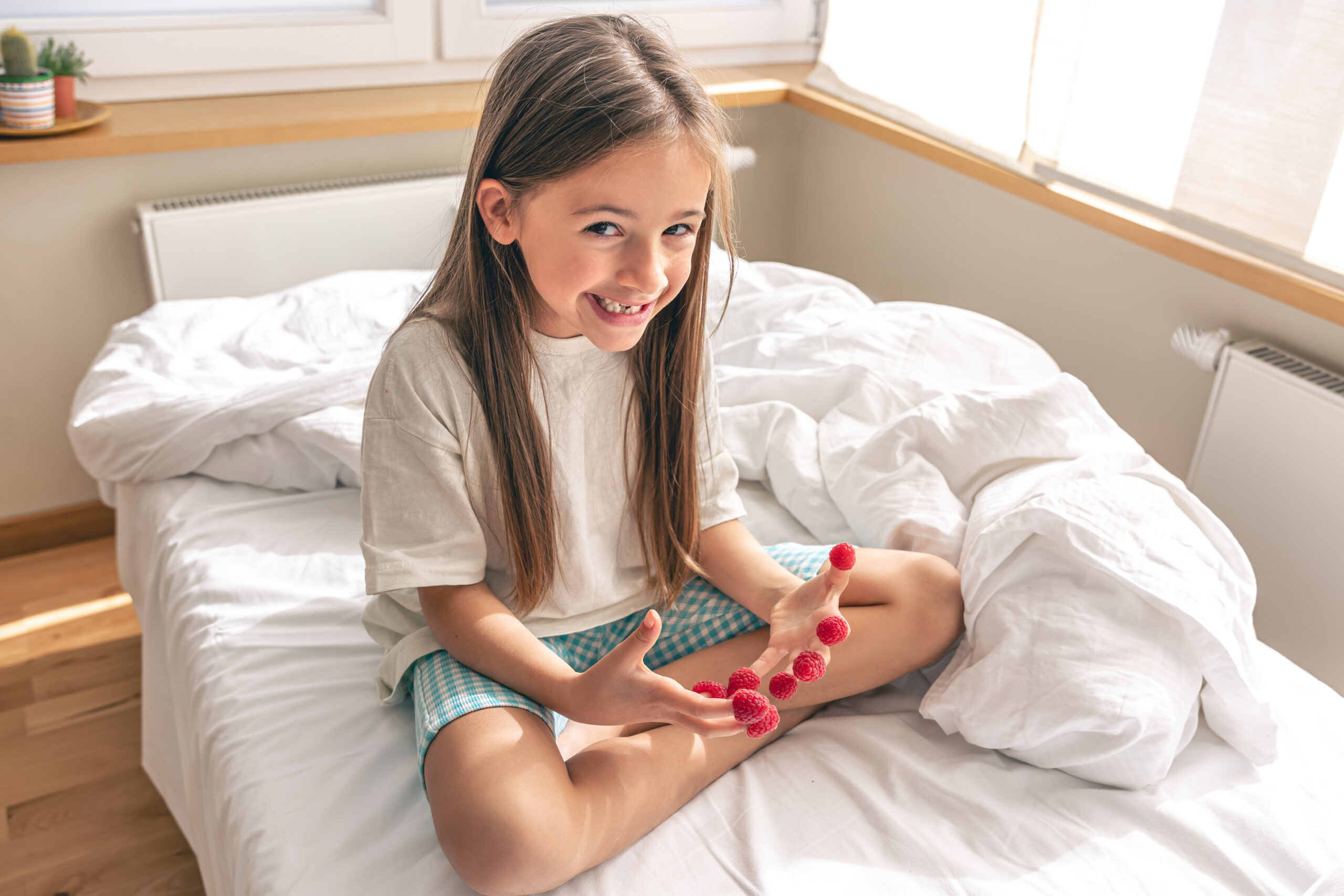Funny little girl with raspberries on her fingers in bed in the morning.